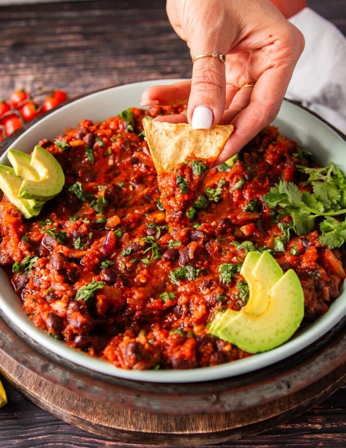 A hand scooping some mexican black beans with chips