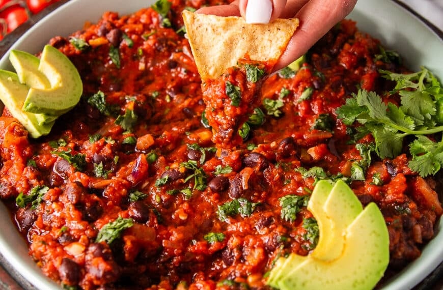 A hand scooping some mexican black beans with chips