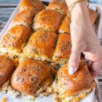 A hand pulling away one chicken slider from the sliders pan
