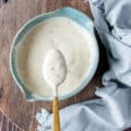 A spoon showing close up texture of coleslaw dressing over a bowl of dressing