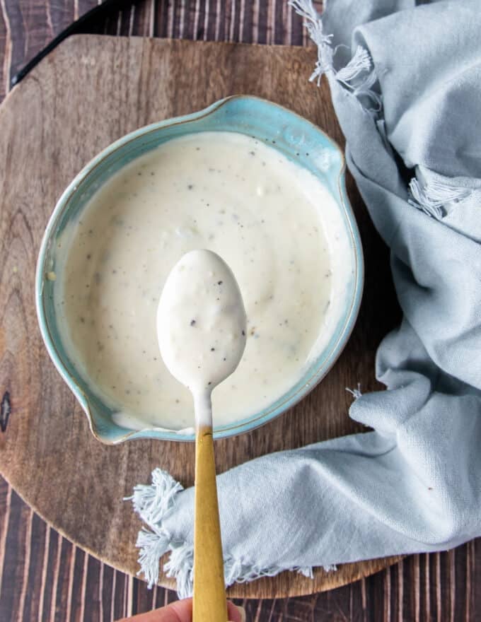 A spoon showing close up texture of coleslaw dressing over a bowl of dressing