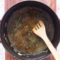 stock, tomatoes, herbs are added to the dutch oven to create the liquid for slow cooking lamb shanks
