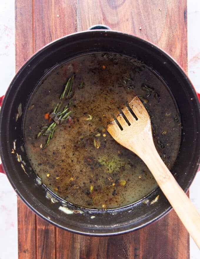 stock, tomatoes, herbs are added to the dutch oven to create the liquid for slow cooking lamb shanks