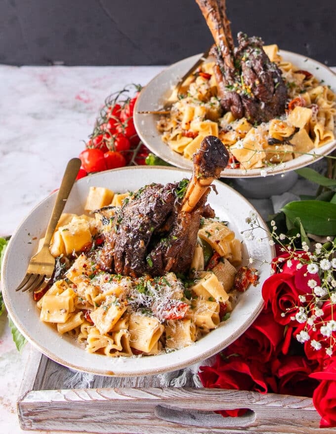 two plates of slow cooked lamb shanks with a succulent sauce over paasta