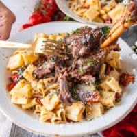 A fork breaking apart a slow cooked lamb shank over pasta showing how fall of the bone it is