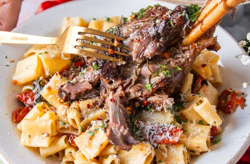 A fork breaking apart a slow cooked lamb shank over pasta showing how fall of the bone it is