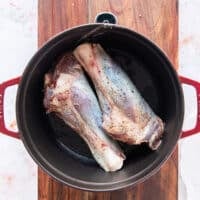 seasoned lamb shanks searing in a Dutch oven over high heat