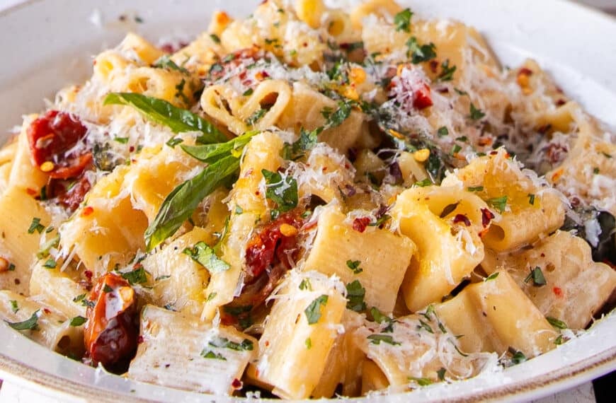 sun dried tomato pasta on a plate with lots of fresh parmesan and basil to garnish
