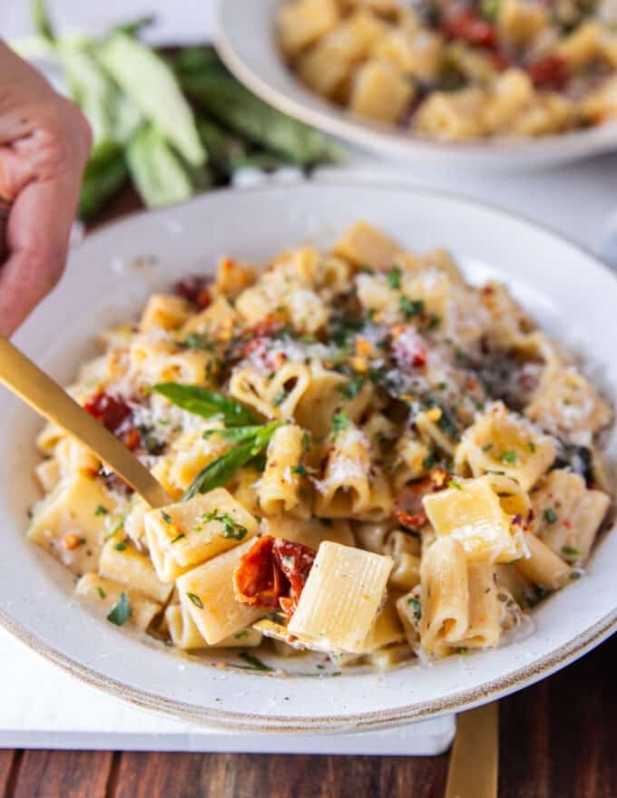 close up of a hand scooping some creamy sun dried tomato pasta sauce with a fork 