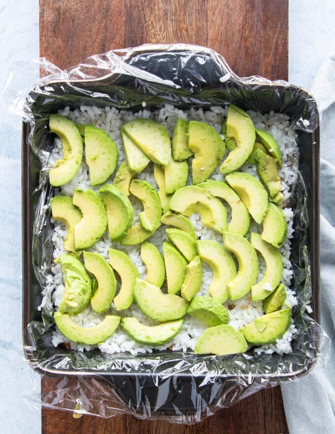 the fist layer of filling of the sushi cake is avocado so a thinly sliced layer of avocado is arranged over the rice