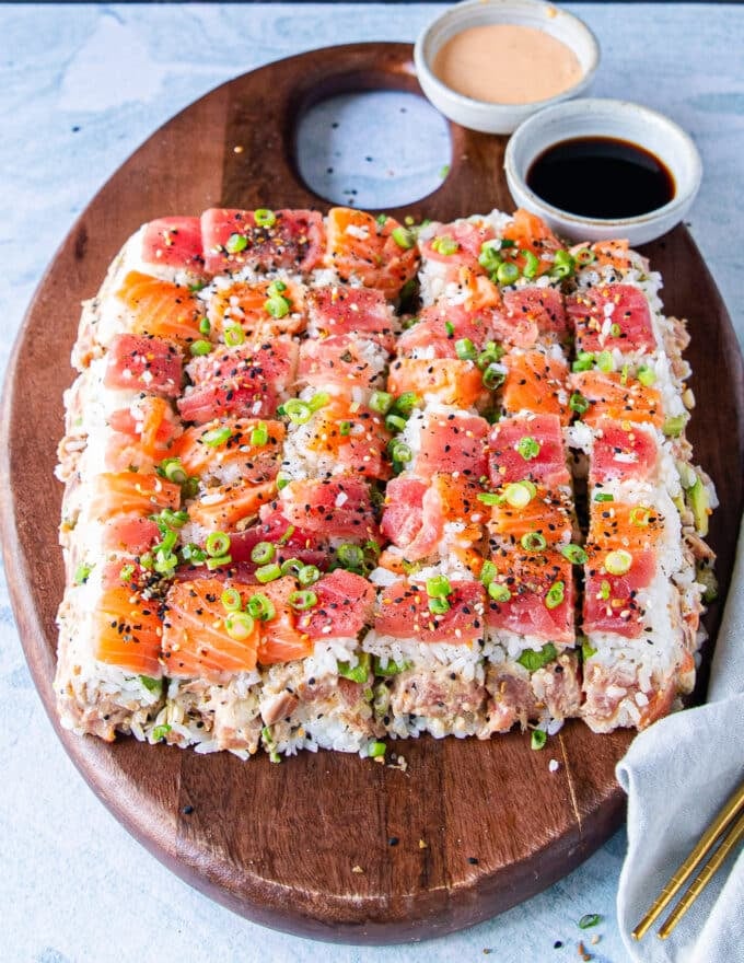 inverted and decorated sushi cake that's cut into small pieces so it's easy to eat and grab garnished with green onions and furikake