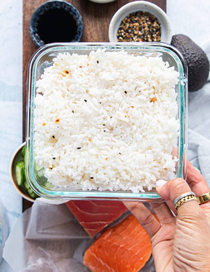 a hand holding ready cooked ans seasoned sushi rice in a bowl ready to use