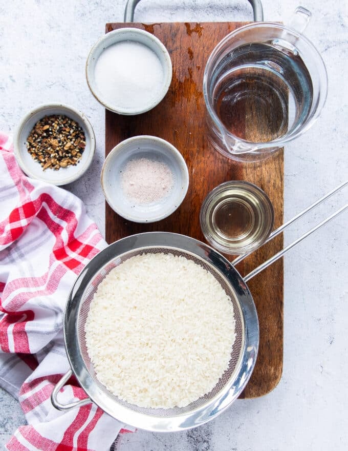 All ingredients needed to make sushi rice from scratch at home including small bowls of seasoning ingredients and Japanese short grain rice