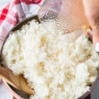 seasoning is poured over the cooked sushi rice in a large bowl to season the rice