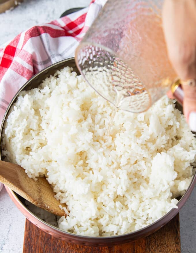 seasoning is poured over the cooked sushi rice in a large bowl to season the rice