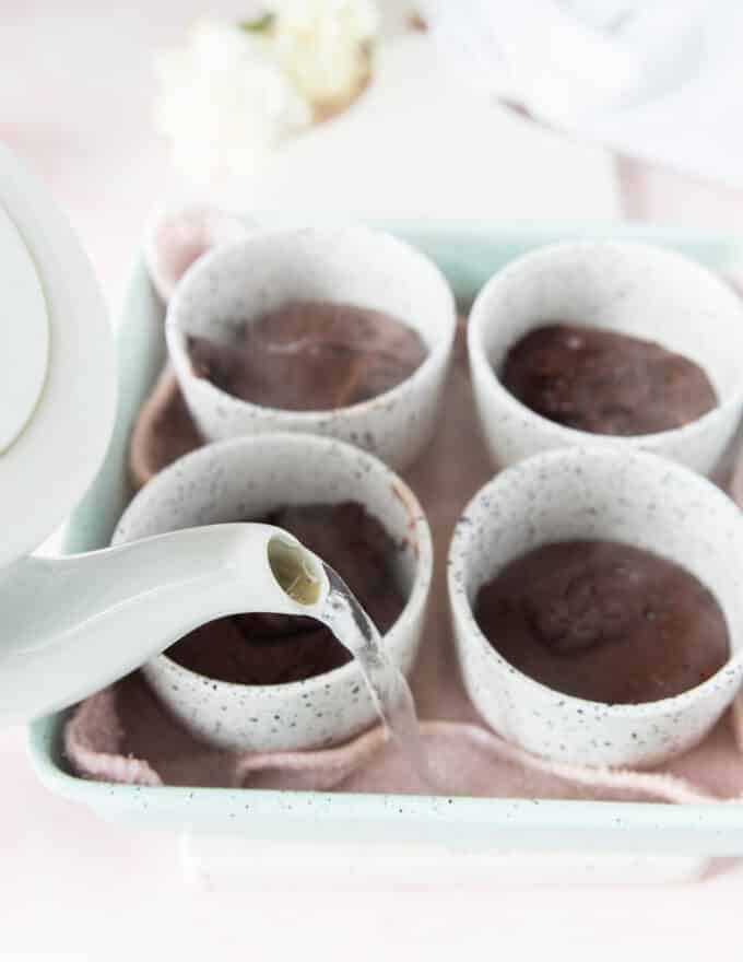 hot boiling water from a kettle being poured in the baking dish to form a water bath