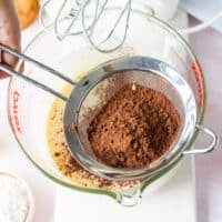 Cocoa powder being sifted over the bowl of light and fluffy eggs and sugar mixture