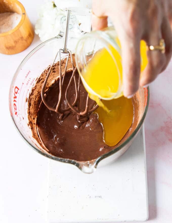melted and cooled butter is slowly drizzled to the side of the bowl to finish the brownie batter 