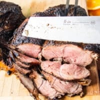 A sharp knife slicing a butterflied leg of lamb showing the perfectly cooked lamb