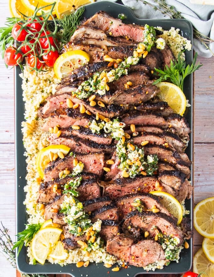 A fully plated butterflied leg of lamb on a plate with a feta herb dressing