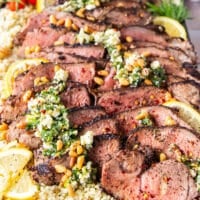 side view of a sliced butterflied leg of lamb and feta herbs dressing all over it