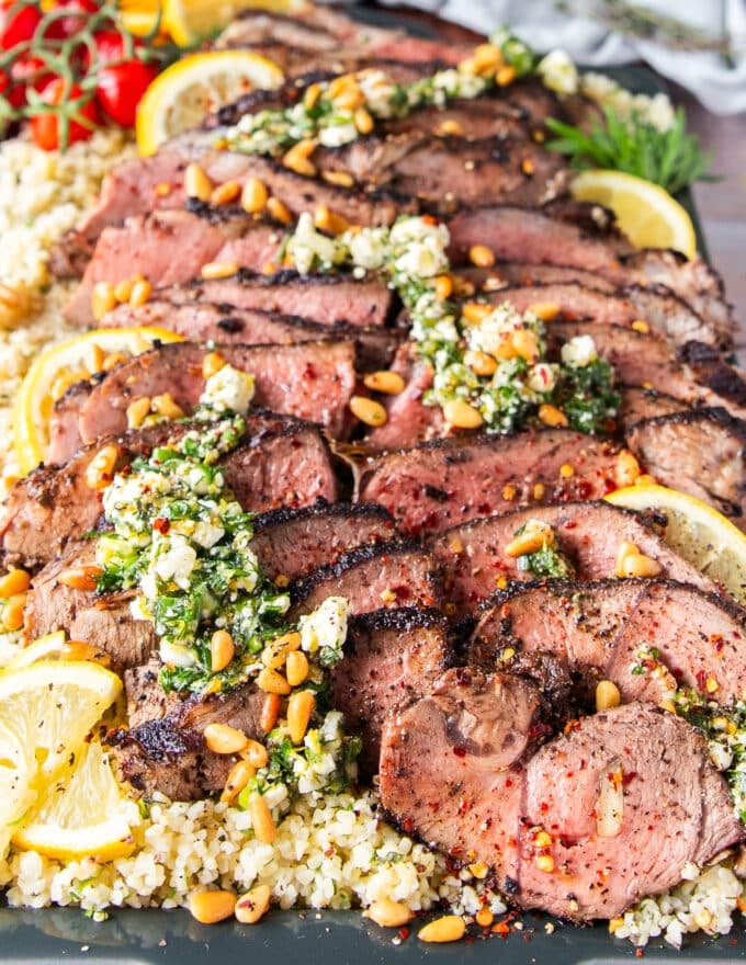 side view of a sliced butterflied leg of lamb and feta herbs dressing all over it