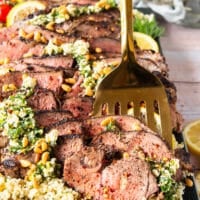 A spoon holding up a slice of butterflied leg of lamb close up showing the perfectly cooked butterflied leg of lamb