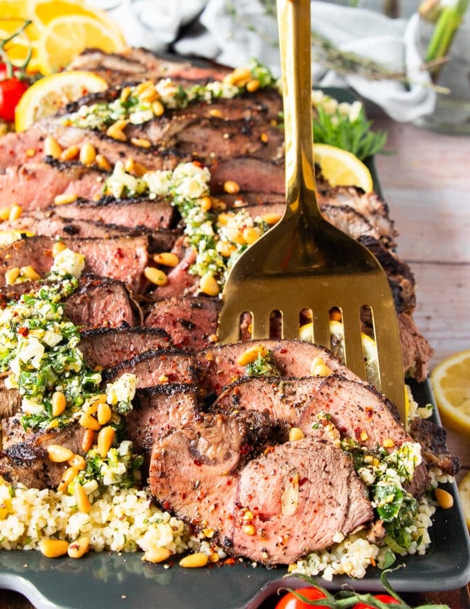 A spoon holding up a slice of butterflied leg of lamb close up showing the perfectly cooked butterflied leg of lamb 