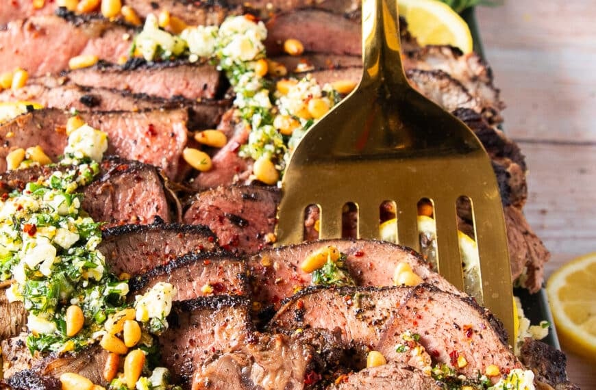 A spoon holding up a slice of butterflied leg of lamb close up showing the perfectly cooked butterflied leg of lamb