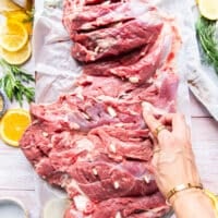 garlic slices being inserted along the leg of lamb to infuse with flavor