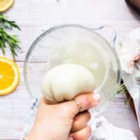 A hand squeezing the water out of the grated onion in the kitchen towel