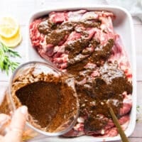 the lamb marinade being poured over the lamb in a shallow dish