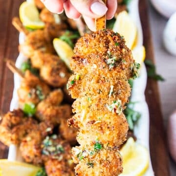 A hand holding one chicken spiedini close up showing the crunchy chicken and lemony butter drizzle on a skewer