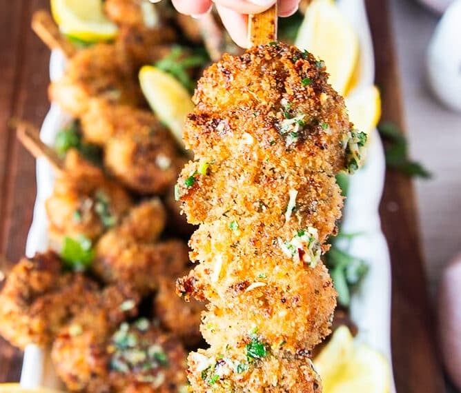 A hand holding one chicken spiedini close up showing the crunchy chicken and lemony butter drizzle on a skewer