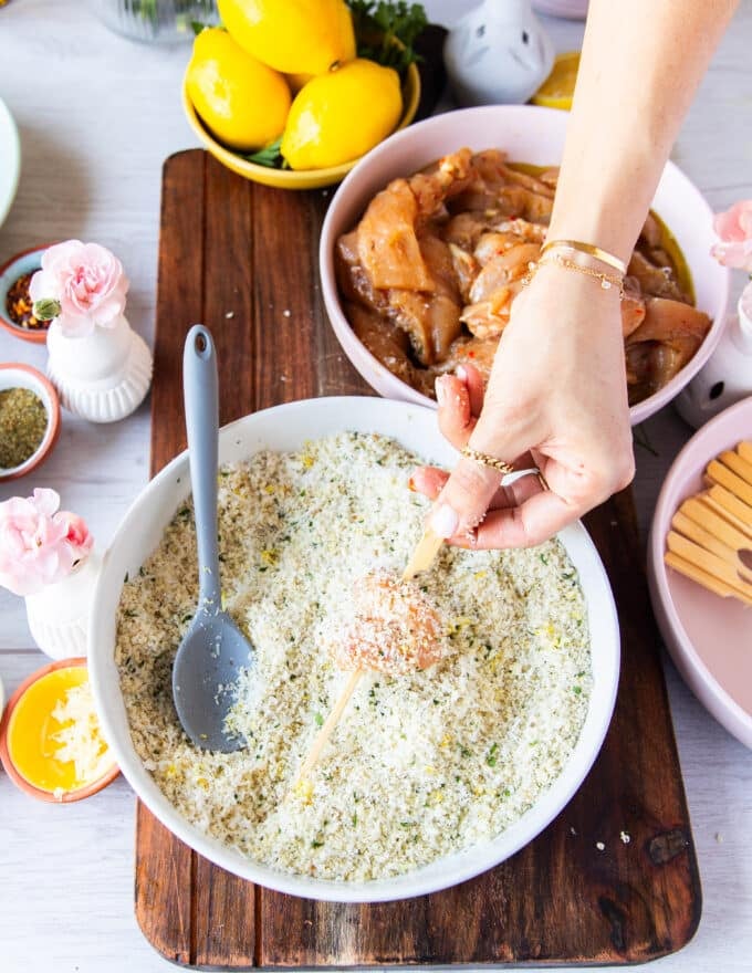 chicken pieces coated in bread crumbs pressed down and being skewered for chicken spiedini