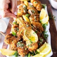 A spoonful drizzling some garlic herb lemon butter over the cooked chicken spiedini on a platter