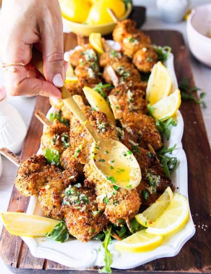 A spoonful drizzling some garlic herb lemon butter over the cooked chicken spiedini on a platter 