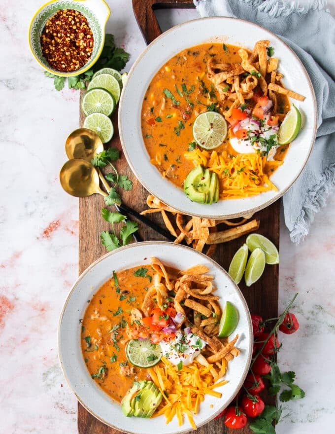 two bowls of chicken taco soup loaded with toppings on a serving board