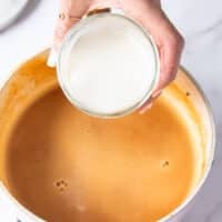 A hand adding cream to a blended soup