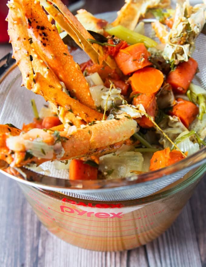 crab stock being strained over a mesh strainer showing the clear seafood broth underneath