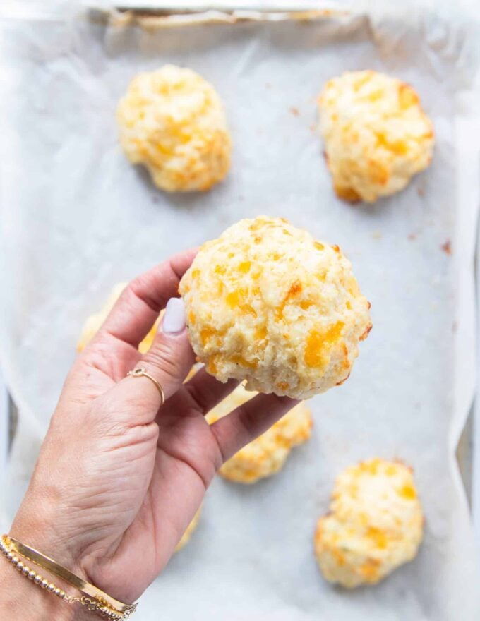 A hand holding one drop biscuit fresh out of the oven close up showing the perfect golden brown and fluffy texture