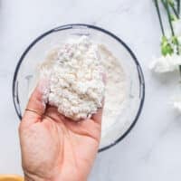 A hand holding the butter when its mixed into the flour mixture showing the pea sized chunks of butter