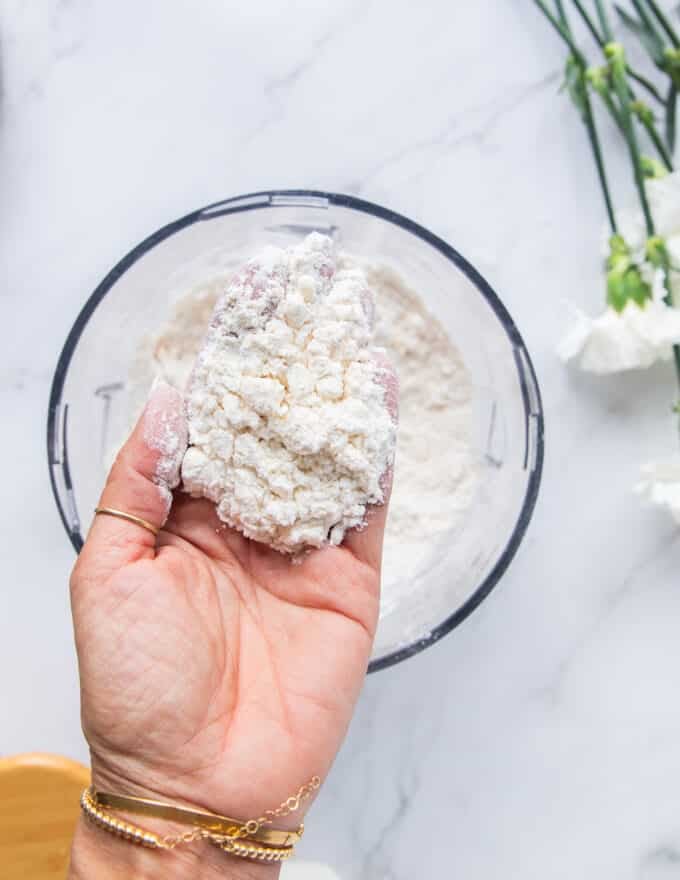 A hand holding the butter when its mixed into the flour mixture showing the pea sized chunks of butter