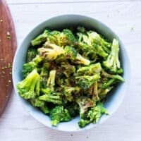 frozen broccoli florets are in a large bowl tossed with seasoning and oil to prepare for air frying