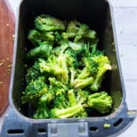 Seasoned frozen broccoli florets in the air fryer basket in a single layer