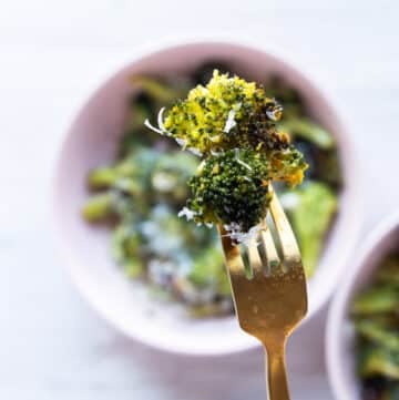 A fork holding an air fryer broccoli piece close up showing the crisp and perfectly cooked broccoli
