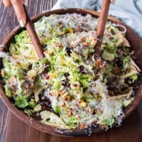 two wooden spoons scooping some Brussel sprout salad with parmesan and walnuts on top
