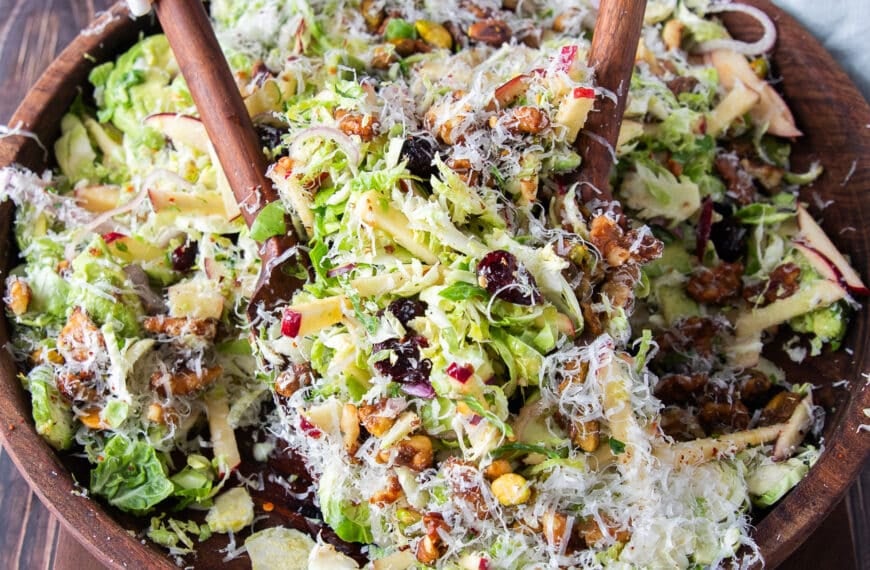 two wooden spoons scooping some Brussel sprout salad with parmesan and walnuts on top