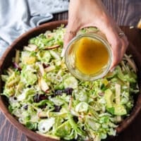 A hand pouring the salad dressing over the salad