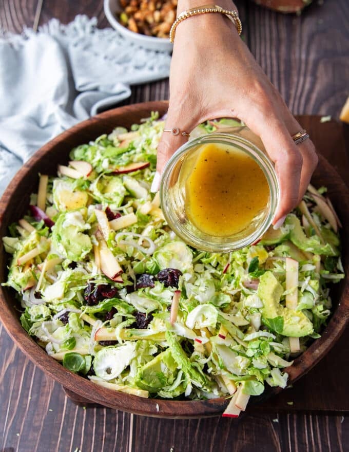 A hand pouring the salad dressing over the salad